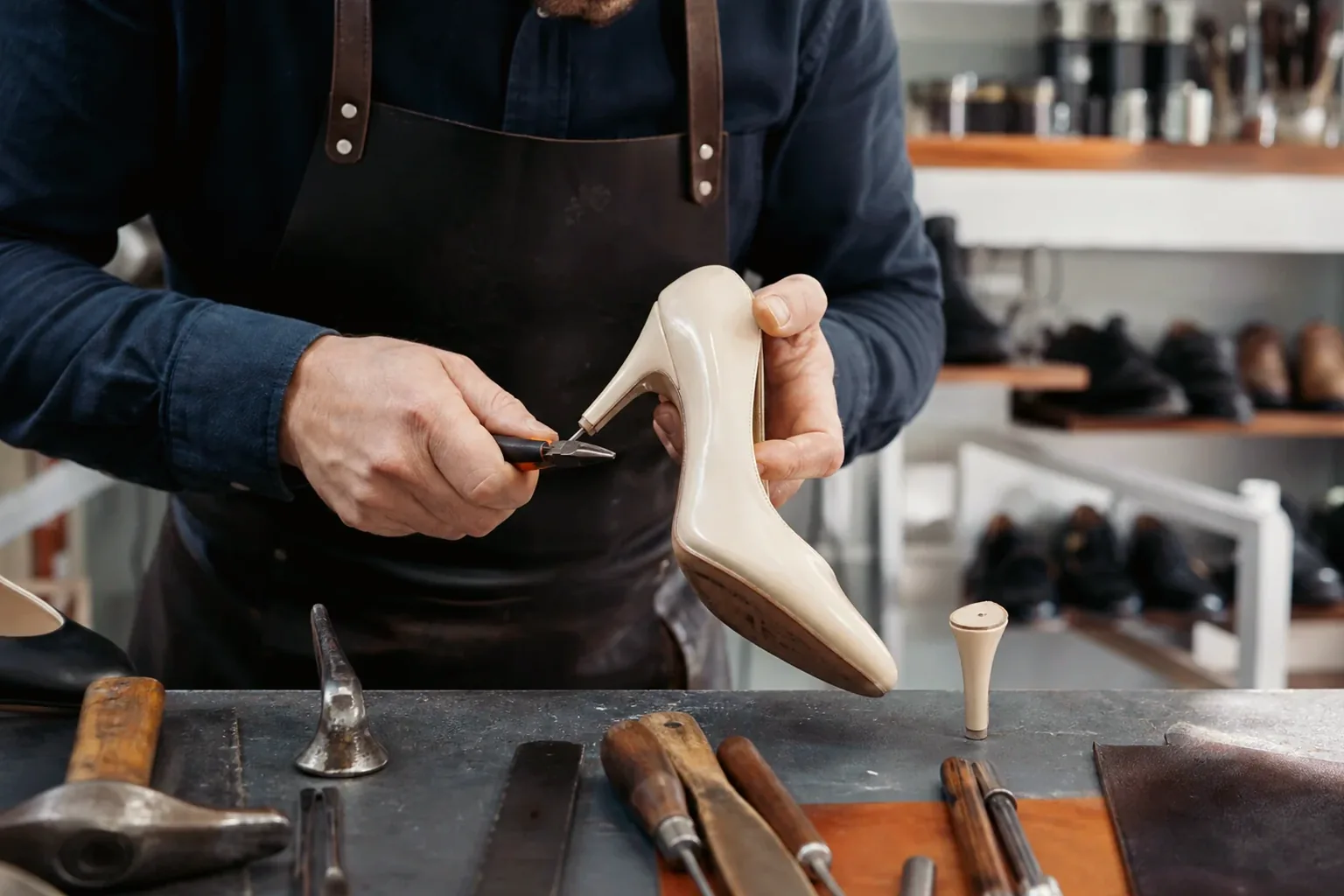 Sapateiro trocando salto de um sapato, com ferramentas e material de trabalho.